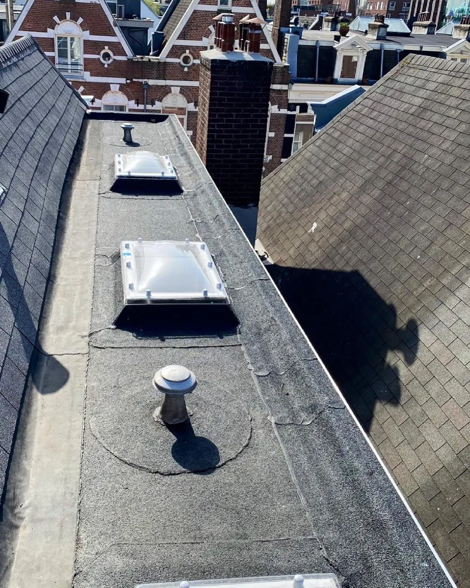 Plat dak met drie lichtkoepels, met daarachter Amsterdamse gevels
