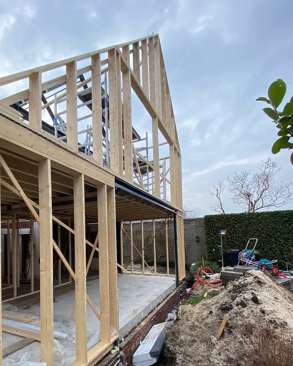 Houten skelet van een aanbouw met puntkap tegen een wolkenlucht